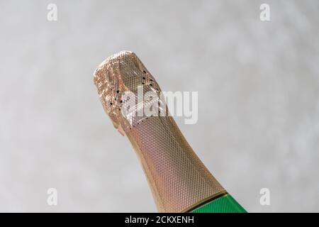 Hals einer geschlossenen Flasche Champagner, verpackt in goldenem Papier auf hellem Hintergrund Stockfoto