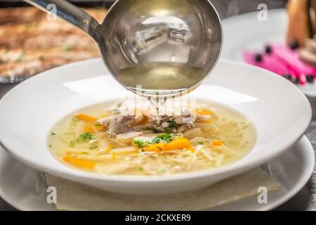 Hühnerbrühe aus der Pfanne in eine Suppe gegossen Eine Platte Stockfoto