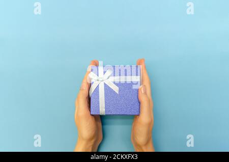 Draufsicht auf Frauen Hände halten eine glänzende dunkelblaue Geschenkbox mit einer weißen Schleife auf einem blauen Hintergrund, Copy Space Stockfoto