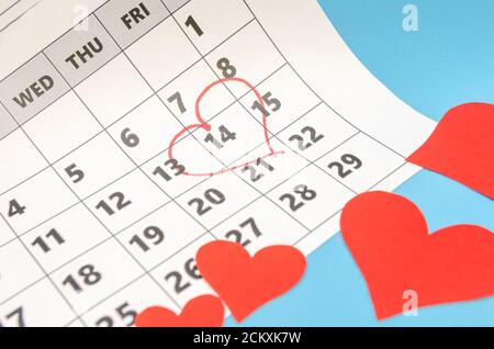 Valentinstag 14 ist mit einem Herz auf dem Kalender markiert, Papierherzen sind verstreut. Urlaubskonzept Stockfoto