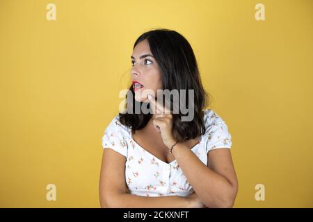 Schöne Frau auf gelbem Hintergrund lächelt und denkt mit den Fingern auf dem Kopf, weil sie eine Idee hat. Stockfoto