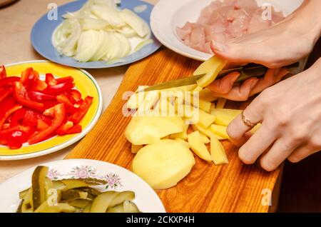 Frauenhänden Kartoffeln in Würfel schneiden, es gibt Schüsseln mit gehacktem Gemüse und Fleisch Stockfoto