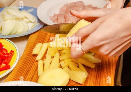 Frauenhänden Kartoffeln in Würfel schneiden, es gibt Schüsseln mit gehacktem Gemüse und Fleisch Stockfoto