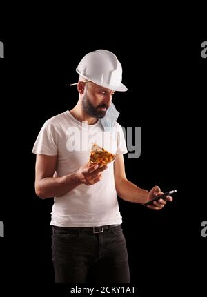 Junger hispanischer Bauarbeiter, der Pizza isst und sein Telefon überprüft Stockfoto