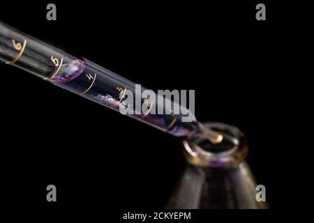 Ein Tropfen blauer Flüssigkeit tropft von der Pipette. Glaszubehör im Labor. Dunkler Hintergrund. Stockfoto