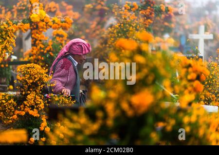 Eine mexikanische indigene Frau geht während der Feierlichkeiten zum Tag der Toten in Ayutla, Mexiko, durch die mit Blumen geschmückten Gräber eines Friedhofs. Stockfoto