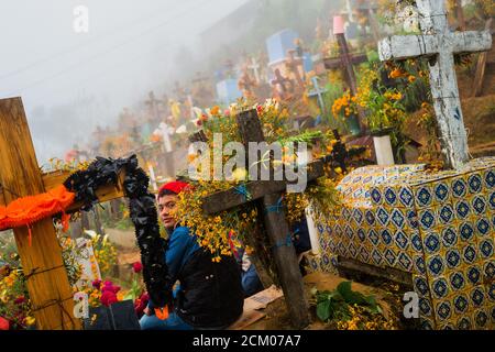 Ein mexikanischer Junge sitzt auf einem mit Blumen geschmückten Grab auf einem Friedhof während der Feierlichkeiten zum Tag der Toten in Ayutla, Mexiko. Stockfoto