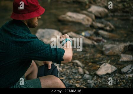 Erkunden, Expeditionskonzept. Angesehene Forscher in Red hat wandern in einem wilden Sommerwald, sitzen auf felsigen Boden und schauen auf Hand w Stockfoto