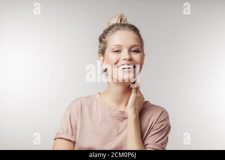 Positive attraktive junge Frau lässig gekleidet, mit Haaren müde im Knoten, lächelnd an der Kamera über weißem Hintergrund mit Copyspace für Werbung. Stockfoto