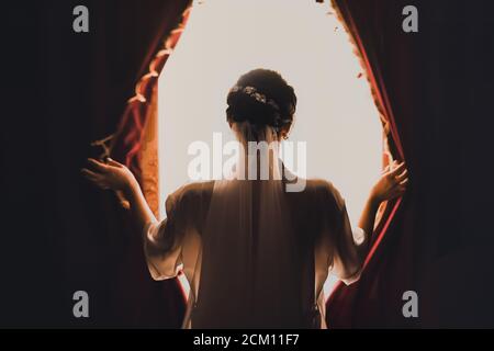 Die Braut öffnet die Vorhänge auf dem riesigen weißen Fenster Stockfoto