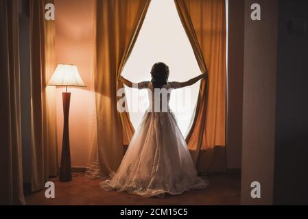 Die Braut öffnet die Vorhänge auf dem riesigen weißen Fenster. Stockfoto