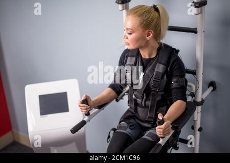 Müde erschöpft und verschwitzt fit Mädchen in EMS-Kostüm versucht, in den Bars zu trainieren. Close up Seitenansicht Foto. Müdigkeit Konzept. Intensives Training Stockfoto