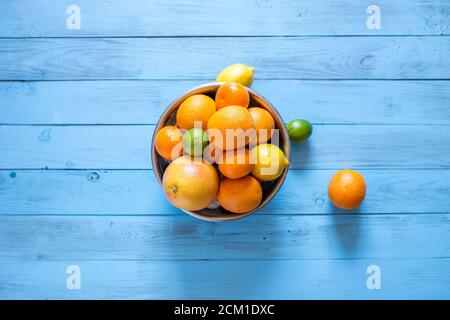 High-Angle-Ansicht von bunten reifen ganzen Zitrusfrüchten wie Orangen, Mandarinen, Limetten, Grapefruits und Zitronen in einer Schüssel auf einem blauen Holzhintergrund mit Stockfoto