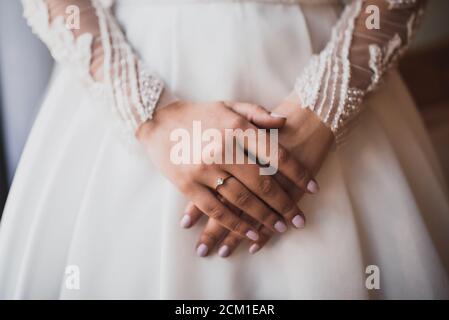 Die weiblichen Hände der hellhäutigen Braut liegen auf dem Weißes Hochzeitskleid Stockfoto