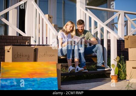Junges Paar mit Buch sitzt auf der Treppe beim Einzug Neues Zuhause Stockfoto