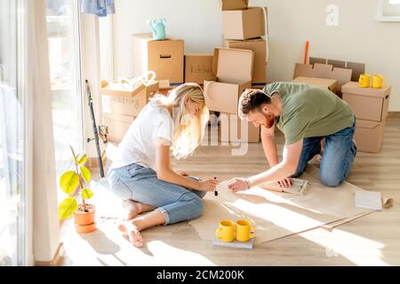 Junges Paar Sitzen am Boden in die neue Heimat auf der Suche nach Grundrissen zusammen Stockfoto
