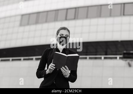 Schöne Geschäftsfrau in einem schwarzen Anzug in einer schwarzen medizinischen Maske und Handschuhe in der Stadt in Quarantäne und Isolation. Pandemie COVID-19. Bild mit sele Stockfoto