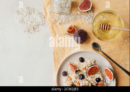 Gesundes Vitaminfrühstück, Haferbrei Haferbrei, Heidelbeeren, frische Feigen und Sanddorn auf gelber Baumwollserviette, Honigstock und langer Löffel, selektiv Stockfoto