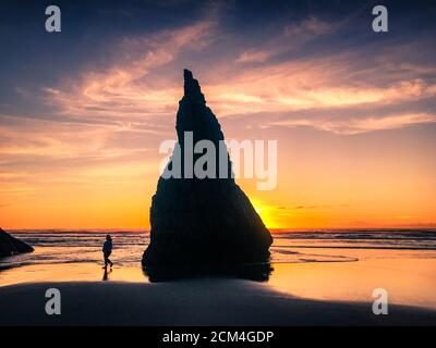 Der Tourist am Oregon Beach spaziert bei Sonnenuntergang am riesigen Meeresstapel vorbei. Stockfoto