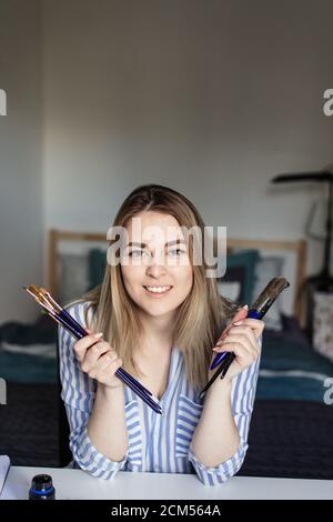 Portrait des blonden Mädchen schreibt mit Pinsel und Tinte und Blick auf Kamera, lettring Prozess Stockfoto