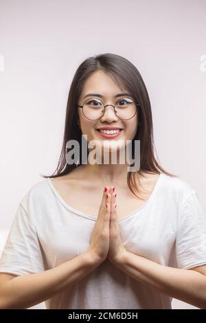 Gastfreundliche asiatische junge Hausfrau, die ihre Gäste trifft, lächelt mit buddhistischer Geste über der Brust an der Kamera, hält die Handflächen zusammen und beugt sich, steht Ov Stockfoto