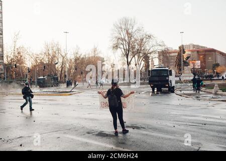 SANTIAGO, CHILE - 11. SEPTEMBER 2020 - EINE junge Frau protestiert mit einem Schild neben einem Polizeifahrzeug. Hunderte von Menschen kamen auf die Plaza Baquedano zu Stockfoto