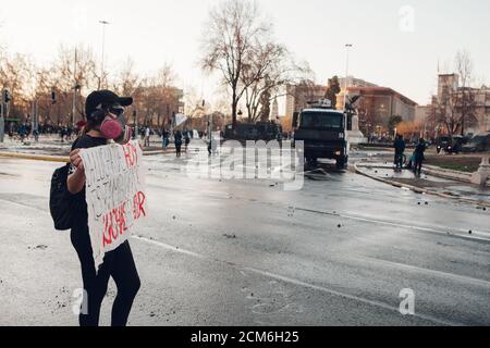 SANTIAGO, CHILE - 11. SEPTEMBER 2020 - EINE junge Frau protestiert mit einem Schild neben einem Polizeifahrzeug. Hunderte von Menschen kamen auf die Plaza Baquedano zu Stockfoto