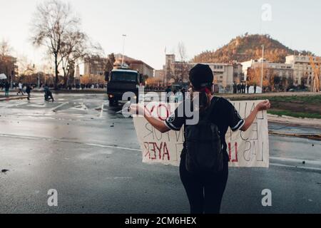 SANTIAGO, CHILE - 11. SEPTEMBER 2020 - EINE junge Frau protestiert mit einem Schild neben einem Polizeifahrzeug. Hunderte von Menschen kamen auf die Plaza Baquedano zu Stockfoto