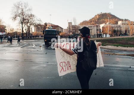 SANTIAGO, CHILE - 11. SEPTEMBER 2020 - EINE junge Frau protestiert mit einem Schild neben einem Polizeifahrzeug. Hunderte von Menschen kamen auf die Plaza Baquedano zu Stockfoto
