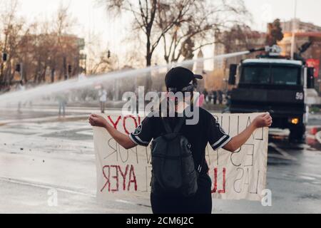 SANTIAGO, CHILE - 11. SEPTEMBER 2020 - EINE junge Frau protestiert mit einem Schild neben einem Polizeifahrzeug. Hunderte von Menschen kamen auf die Plaza Baquedano zu Stockfoto