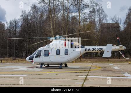 Weißer Hubschrauber auf dem Boden sitzend, vor dem Hintergrund von Bäumen und Gebäuden, horizontal Stockfoto