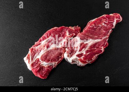 Rohes Schweinefleisch oder Rindfleisch. Frische Steaks auf Schiefertafel auf schwarzem Hintergrund. Draufsicht, Nackenfleisch Stockfoto