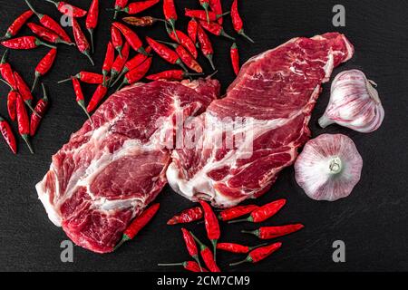 Frische Steaks aus rohem Schweinefleisch auf dunklem Steingrund, Draufsicht, Food-Konzept Stockfoto