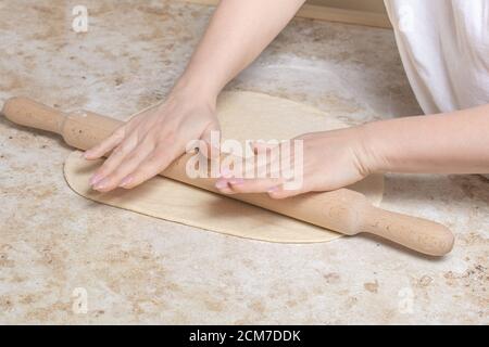 Nahaufnahme der jungen Frau, die Teig mit Holzpfeifholz rollt. Hausfrau macht Pizza zu Hause auf der Küche. Bäckerei, Ernährung. Pizza machen bei ho Stockfoto