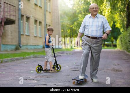 Großvater und Enkel auf einem Spaziergang. Ein Kind sieht seinem Großvater beim Fahren auf einem Skateboard zu. Stockfoto