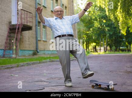 Ein älterer Mann lernt, ein Skateboard zu fahren. Ein moderner Rentner. Stockfoto