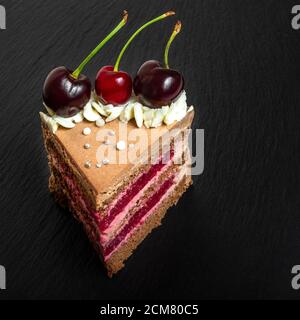 Detail auf einem Stück Schwarzwaldkuchen oder traditionelle schwarzwaldkuchen aus dunkler Schokolade und Sauerkirschen auf schwarzem Tisch Stockfoto