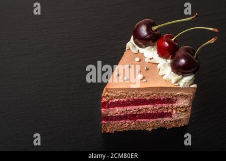Detail auf einer Scheibe Schokolade Karamell Kuchen mit Kirschen auf schwarzem Teller. Copyspace Stockfoto