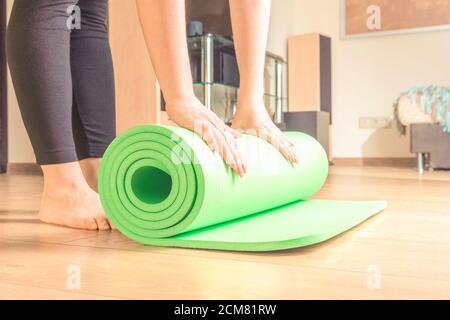 Frau rollt ihre Yogamatte nach einem Training, Yoga online. Ausrüstung für Yoga. Konzept gesunde Lebensweise, Sport und Ernährung. Stockfoto