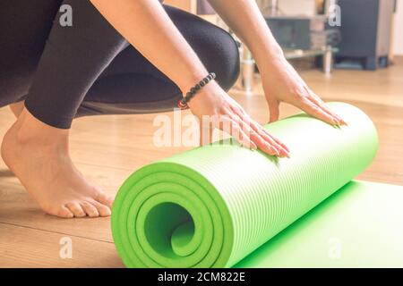 Frau rollt ihre Yogamatte nach einem Training, Yoga online. Ausrüstung für Yoga. Konzept gesunde Lebensweise, Sport und Ernährung. Stockfoto