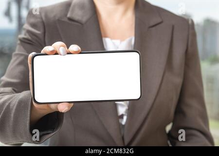 Frauenhand zeigt das Smartphone mit weißem Bildschirm in horizontaler Position. Mock-up-Handy. Stockfoto