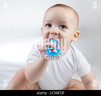 Porträt eines zehn Monate alten Babys mit blauer Rassel im Mund Stockfoto