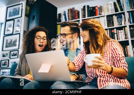 Gruppe glücklicher Studenten, die Bücher lesen und sich auf die Prüfung in der Bibliothek vorbereiten Stockfoto