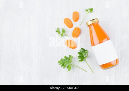 Frischer Orangenkarottensaft in Glasflasche mit Blankoetikett, Zutaten und grünen Blättern auf weißem Holzbrett, Mock up für Design, Werbung, Brandin Stockfoto