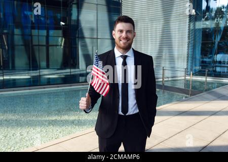 Geschäftsmann steht mit USA Flagge in den Händen. Geschäftsmann mit amerikanischer Flagge im Business Center Stockfoto