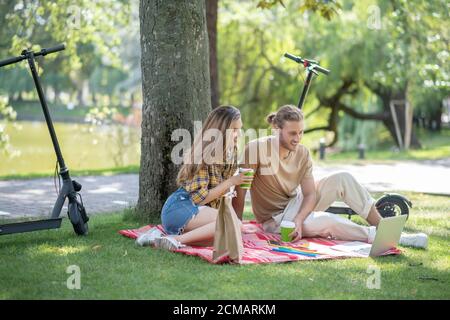 Junges Paar, das unter dem Baum sitzt und etwas auf sieht Notebook Stockfoto