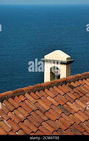 Split Blick auf ein traditionelles Dach einer Kirche mit alten Terrakotta-Fliesen und einer Bronzeglocke und auf den Atlantik, Teneriffa, Kanarische Inseln Stockfoto