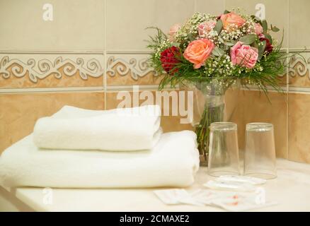 Rustikale Hotelbadezimmer Notwendigkeiten mit einem Satz von weißen Handtüchern, einfache Gläser, Seife und ein Rosenstrauß, Zubehör geeignet für Übernachtung und Frühstück Stockfoto