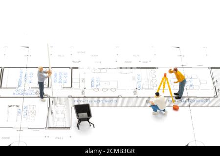 Miniatur Menschen Vermesser Techniker misst die Entfernung, um ein Haus auf Zeichnung Plan zu bauen. Stockfoto