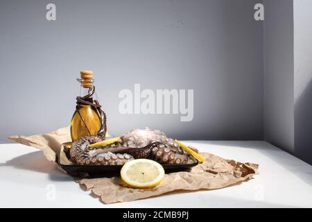 Meeresfrüchte, ganze rohe große Krake auf einem Teller mit Zitronen und Olivenöl bereit für die Vorbereitung, Seitenansicht Stockfoto